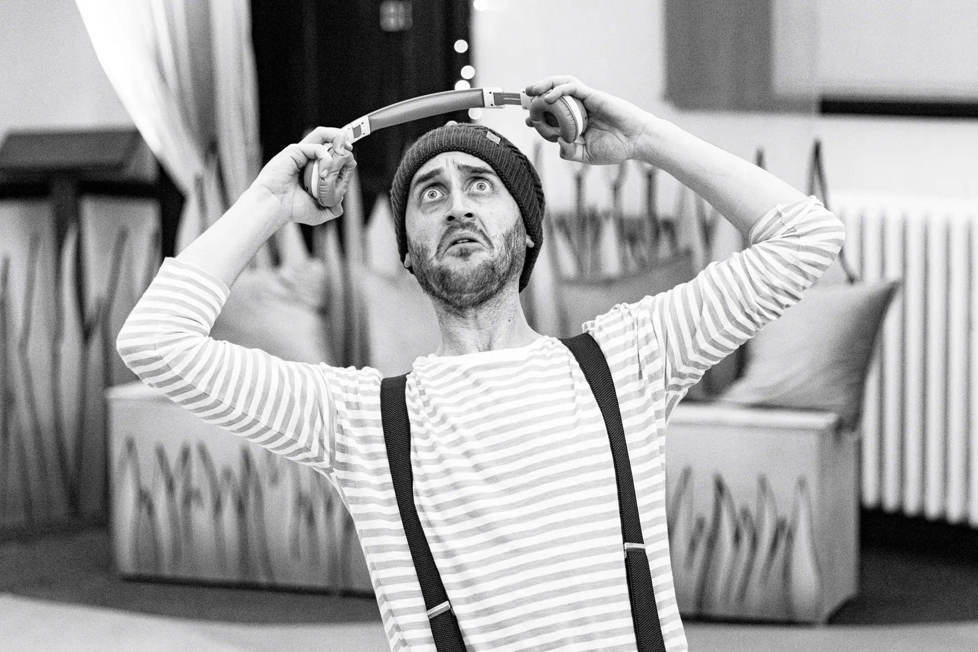 Black and white image of an actor from Spinning Wheel Theatre's 'Five Little Ducks' performance at Ipswich County Library, making a comedic, wide-eyed expression while holding headphones above his head. Captured by Theatre photography specialist, Fourth Wall Photography.