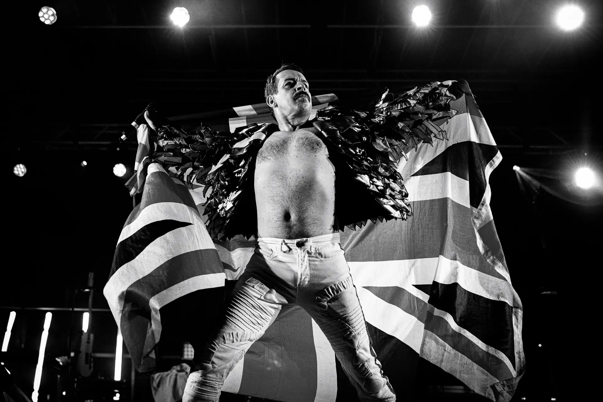 Black and white image of Freddie Mercury tribute from Supersonic Queen on stage, wearing a Union Jack flag as a cape and a winged jacket at the Legends Festival in Cromer. Captured by Live Music photography specialist, Fourth Wall Photography.