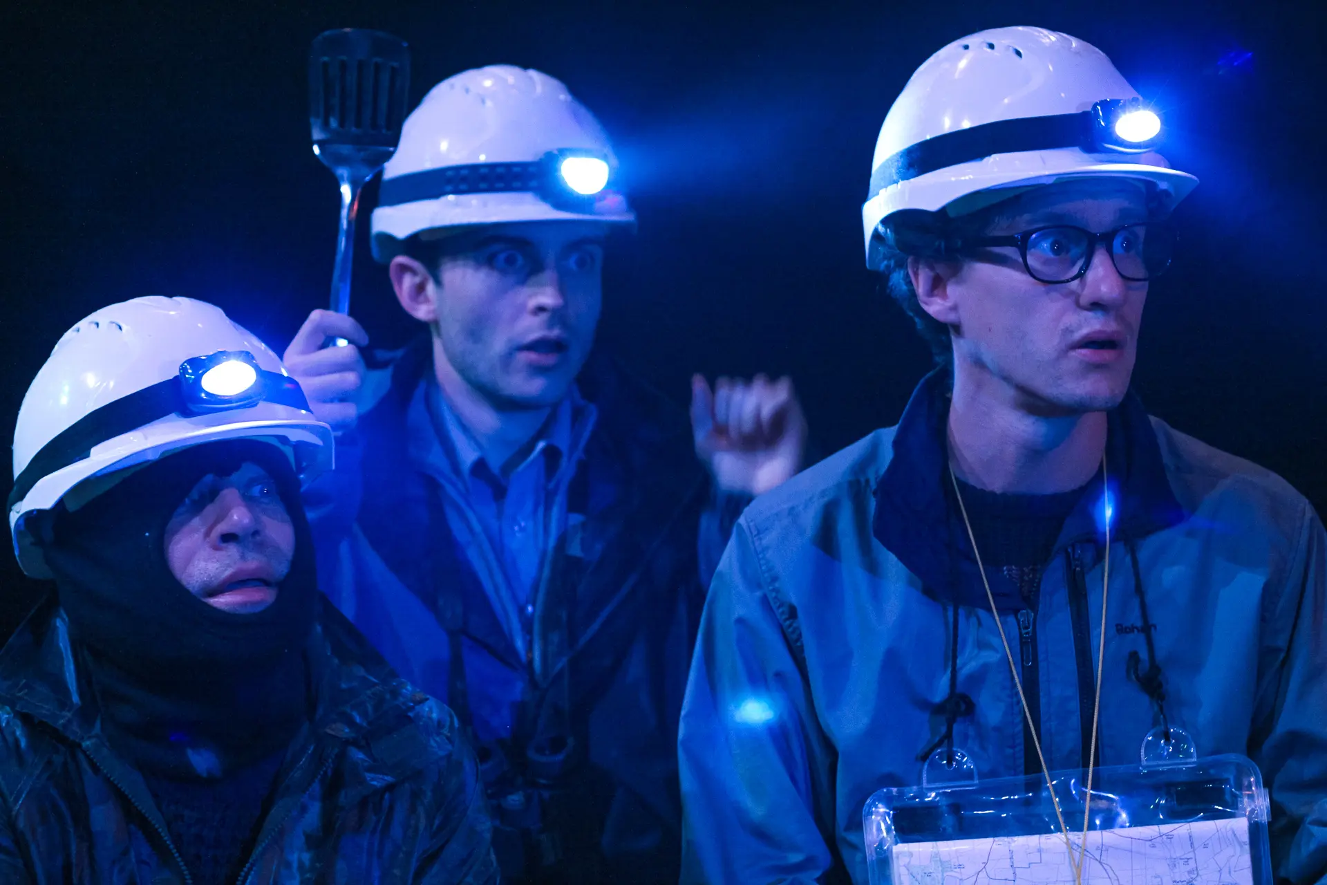 Three male actors wearing hard hats with headlamps, portraying characters from 'Neville's Island' during the summer rep season at Sheringham Little Theatre, looking surprised under blue lighting. Captured by Theatre photography specialist, Fourth Wall Photography.