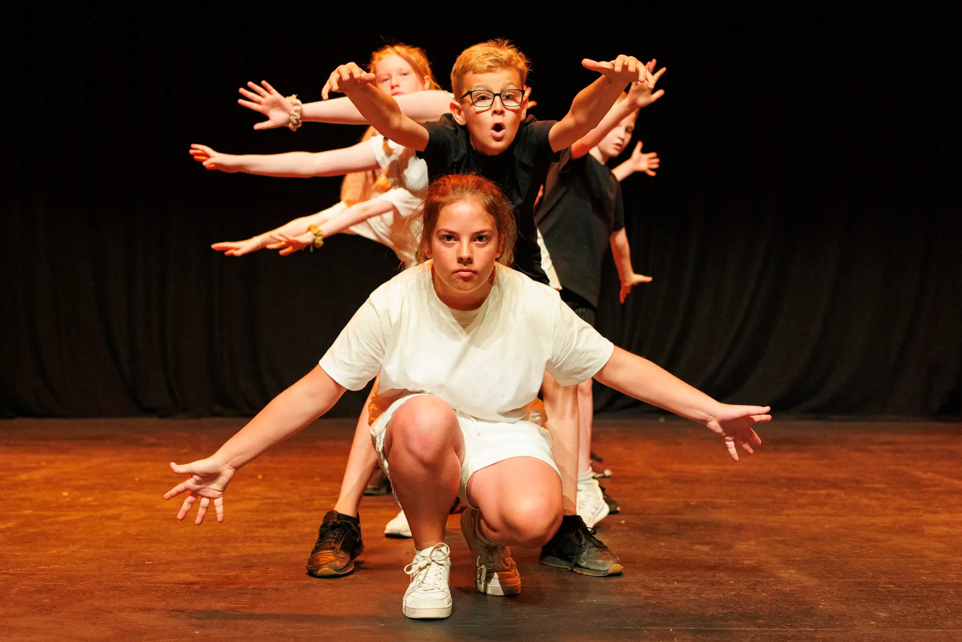 Young dancers performing a routine at the Schools Dance Festival at the Marina Theatre Lowestoft. Captured mid‑movement on stage with vibrant lighting. Captured by Dance photography specialist, Fourth Wall Photography.