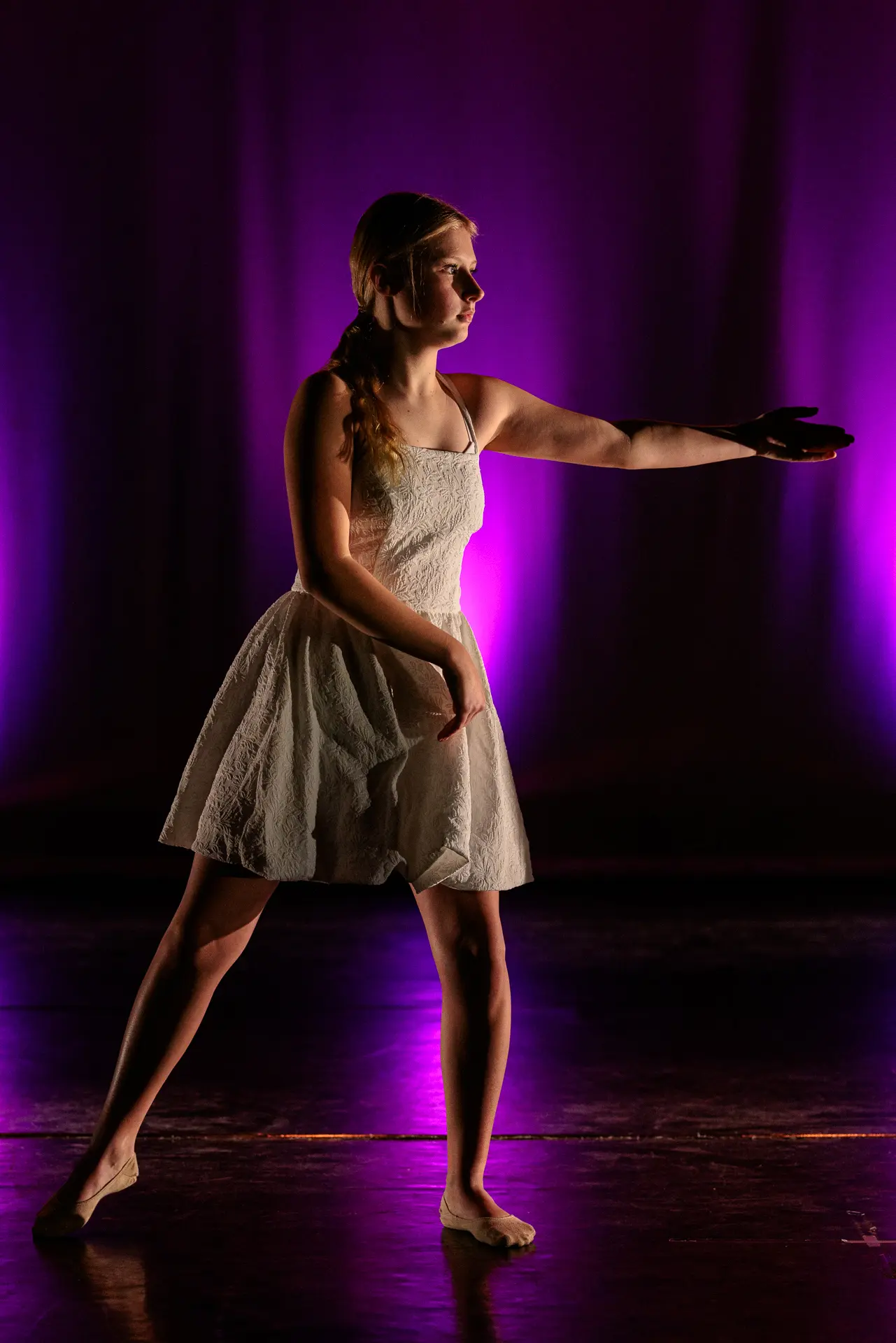 Dancer performing a contemporary dance routine for True Motion Dance in a white dress with purple lighting at the Atrium Theatre, North Walsham. Captured by Dance photography specialist, Fourth Wall Photography.